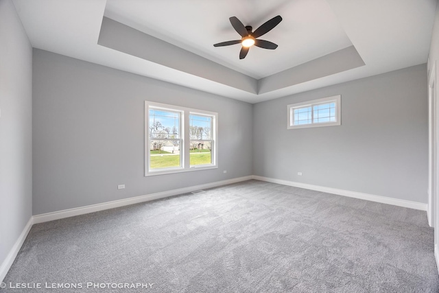 carpeted spare room with baseboards, a ceiling fan, and a tray ceiling