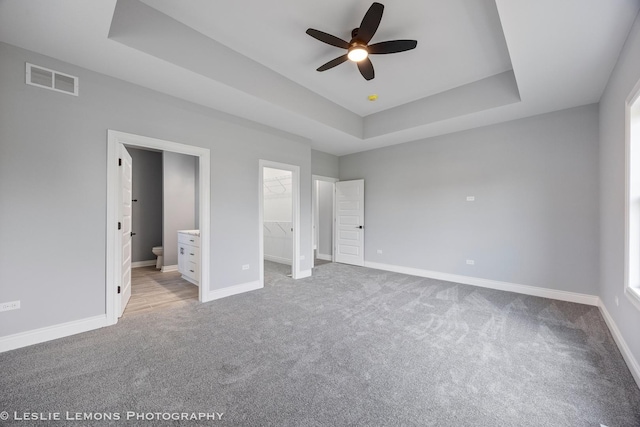unfurnished bedroom with visible vents, a spacious closet, a tray ceiling, and light carpet
