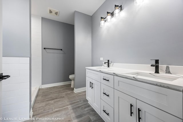 bathroom with baseboards, wood finished floors, toilet, and a sink