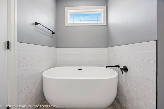 bathroom with tile walls, wainscoting, and a soaking tub