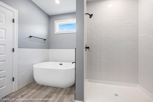 bathroom with tile walls, a tile shower, a wainscoted wall, a freestanding bath, and wood finished floors