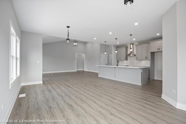 kitchen featuring baseboards, recessed lighting, wall chimney range hood, gray cabinetry, and light wood-type flooring