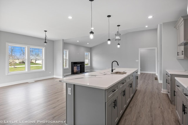 kitchen featuring a kitchen island with sink, a sink, light wood-style floors, baseboards, and gray cabinetry