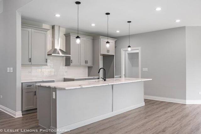 kitchen with a sink, decorative backsplash, gray cabinets, wall chimney range hood, and wood finished floors