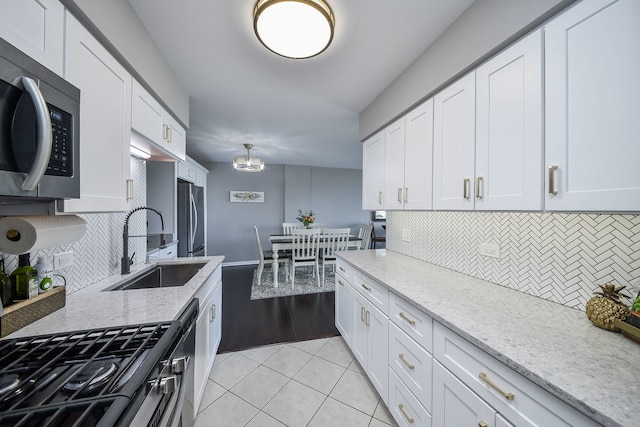 kitchen featuring decorative backsplash, appliances with stainless steel finishes, a sink, light tile patterned floors, and white cabinets