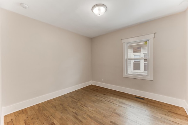 empty room featuring wood finished floors, visible vents, and baseboards