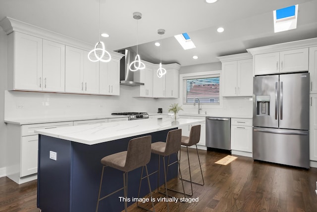 kitchen featuring wall chimney exhaust hood, stainless steel appliances, a skylight, white cabinets, and dark wood-type flooring