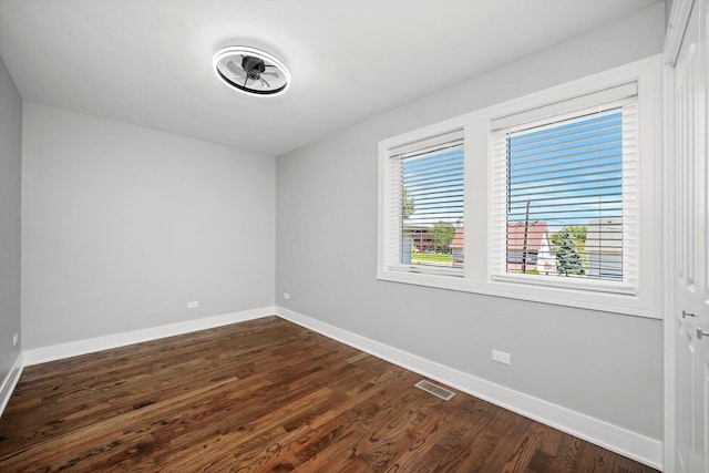 unfurnished room featuring dark wood-style flooring, visible vents, and baseboards