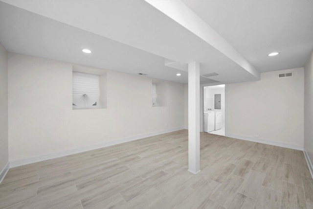 finished below grade area with light wood finished floors, washer and clothes dryer, visible vents, and baseboards