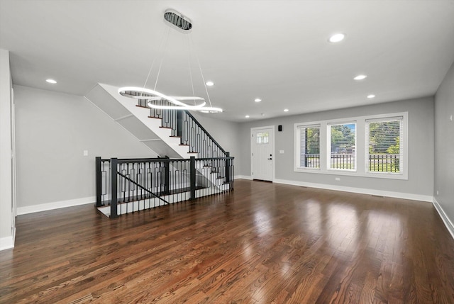 unfurnished living room featuring recessed lighting, wood finished floors, baseboards, and a notable chandelier