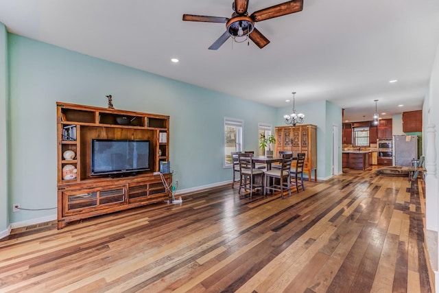 living room with wood-type flooring, recessed lighting, baseboards, and ceiling fan with notable chandelier