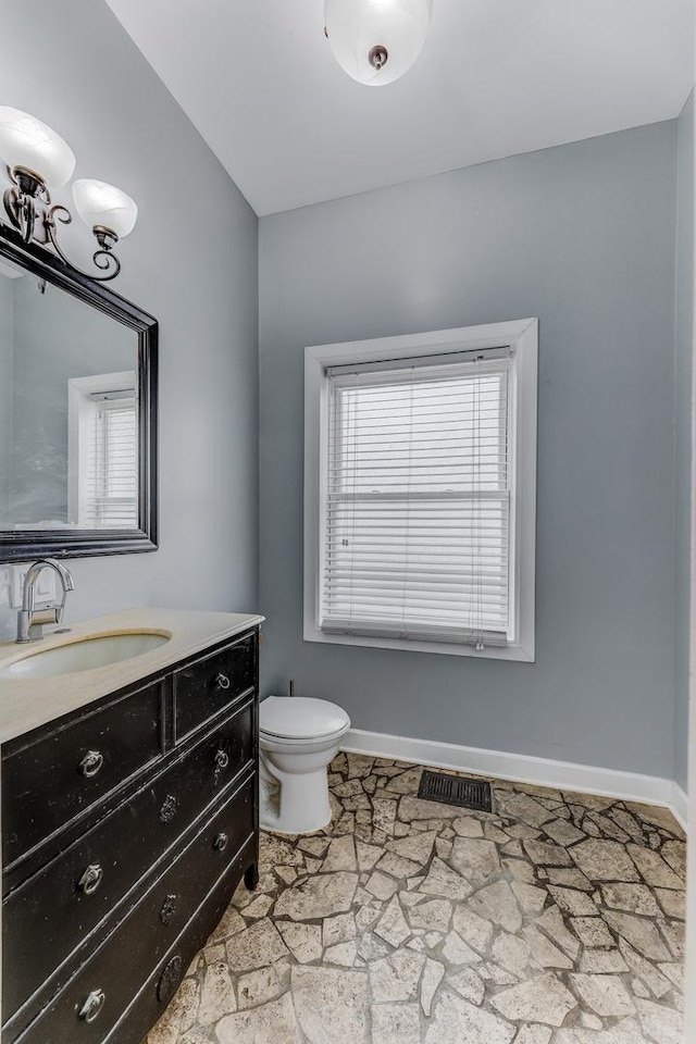 bathroom with vanity, stone finish flooring, toilet, visible vents, and baseboards