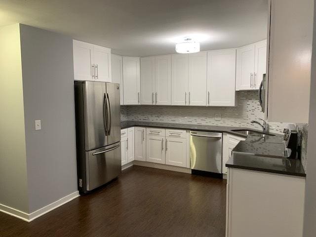 kitchen featuring dark countertops, tasteful backsplash, a sink, dark wood-style floors, and stainless steel appliances