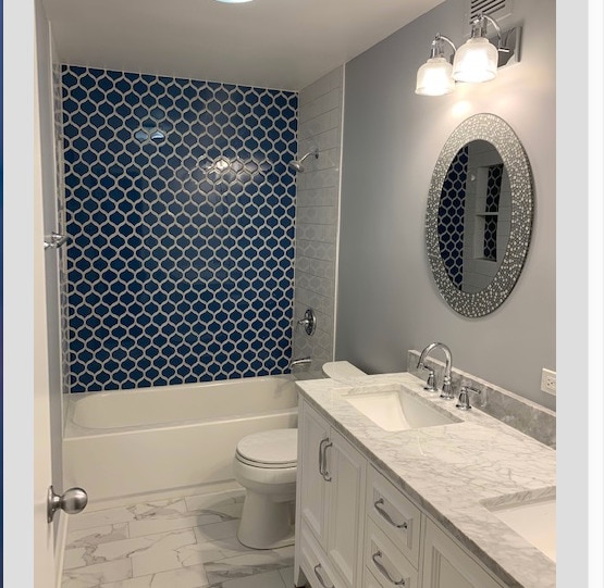 full bath with double vanity, marble finish floor, tub / shower combination, toilet, and a sink