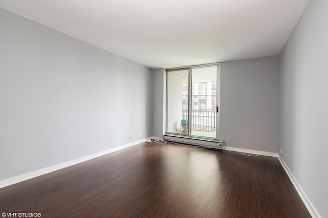 spare room with baseboards, a baseboard heating unit, and dark wood-type flooring