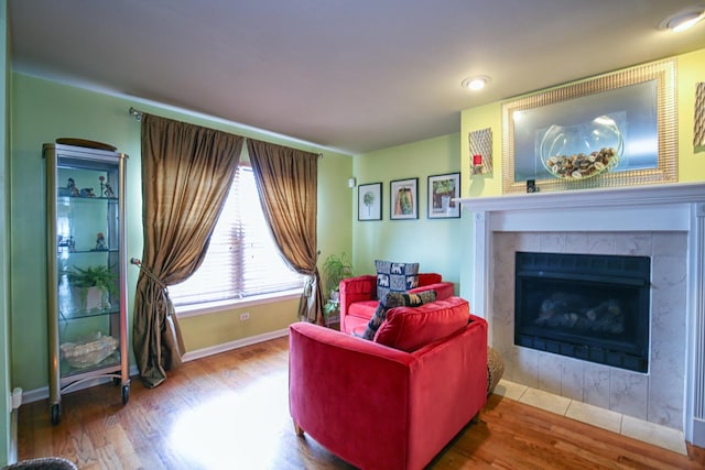 living area with a tiled fireplace, baseboards, and wood finished floors