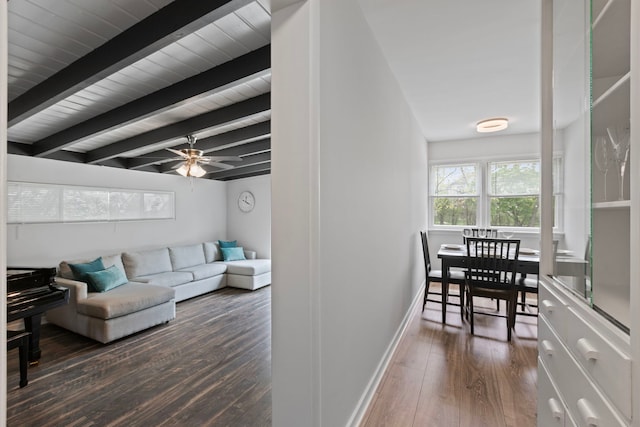 living area with baseboards, dark wood-style flooring, beamed ceiling, and ceiling fan
