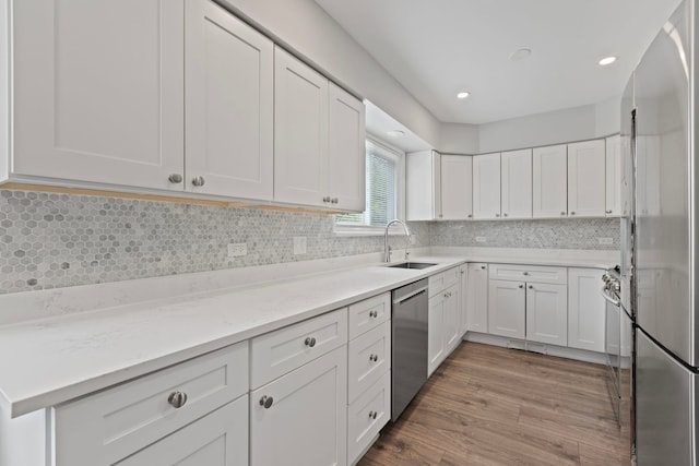 kitchen featuring a sink, wood finished floors, backsplash, white cabinets, and appliances with stainless steel finishes