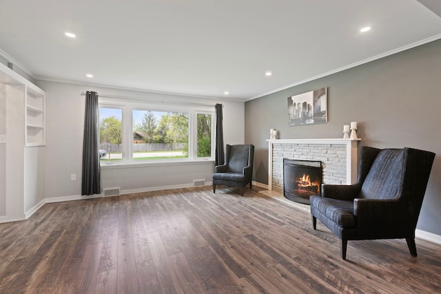 living area with ornamental molding, a stone fireplace, visible vents, and wood finished floors