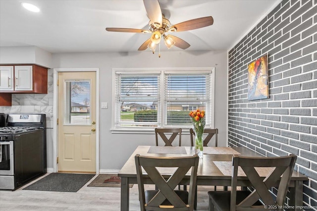 dining area featuring a ceiling fan, baseboards, light wood finished floors, and brick wall