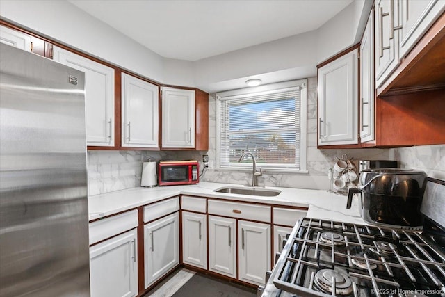 kitchen with decorative backsplash, stainless steel fridge, light stone counters, a sink, and gas stove