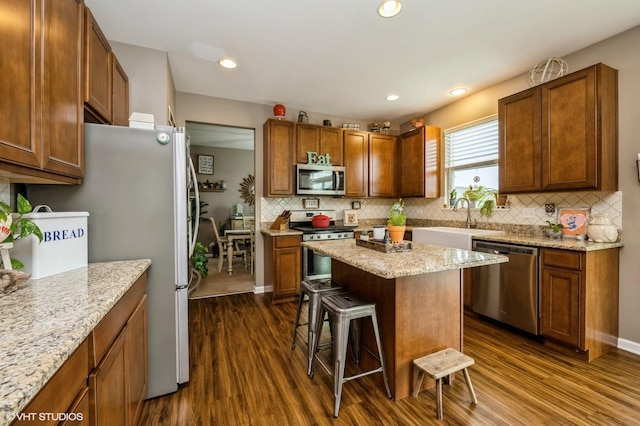kitchen with a kitchen bar, dark wood-style flooring, appliances with stainless steel finishes, tasteful backsplash, and a sink