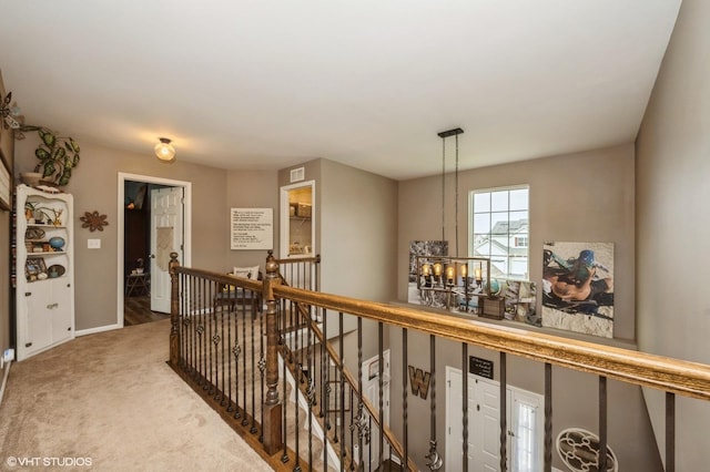 corridor featuring light colored carpet, a notable chandelier, baseboards, an upstairs landing, and visible vents