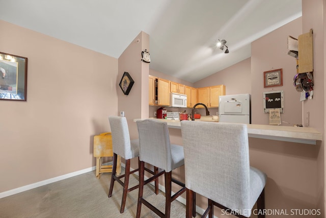 kitchen with carpet floors, light brown cabinetry, white appliances, a kitchen bar, and vaulted ceiling