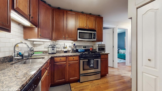 kitchen with backsplash, appliances with stainless steel finishes, a sink, light stone counters, and light wood-style flooring
