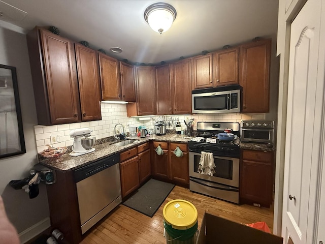 kitchen with light wood-type flooring, a sink, backsplash, and stainless steel appliances
