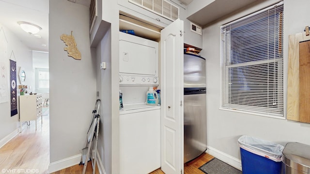 clothes washing area with laundry area, stacked washer and dryer, visible vents, wood finished floors, and baseboards