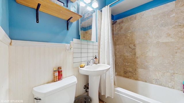 full bath featuring toilet, a sink, shower / bath combo, and a wainscoted wall