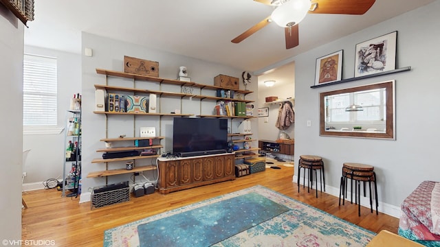 living area with baseboards, a ceiling fan, and wood finished floors