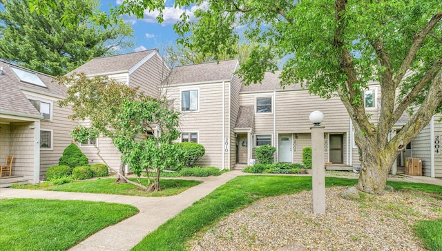multi unit property with roof with shingles and a front lawn