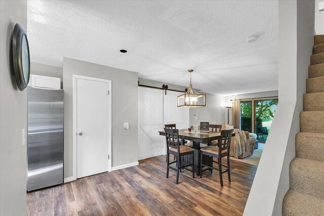 dining area with a textured ceiling, a barn door, wood finished floors, stairway, and baseboards