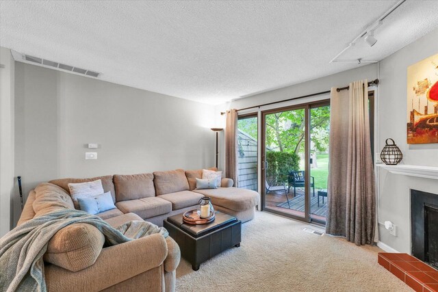 carpeted living area with track lighting, a textured ceiling, visible vents, and a tiled fireplace