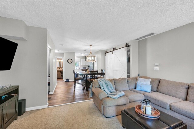 living room featuring light colored carpet, a textured ceiling, visible vents, and a barn door