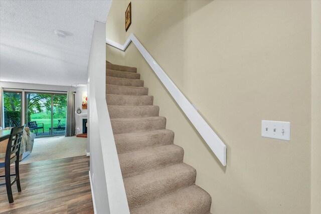 stairs with a fireplace with raised hearth, a textured ceiling, and wood finished floors