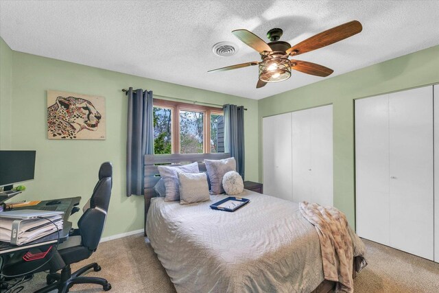 bedroom with ceiling fan, a textured ceiling, visible vents, multiple closets, and carpet flooring