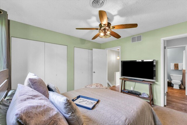 bedroom with two closets, a textured ceiling, ceiling fan, and visible vents