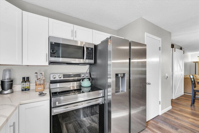 kitchen with white cabinets, appliances with stainless steel finishes, wood finished floors, and light stone counters