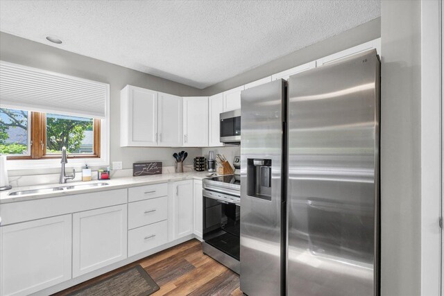 kitchen featuring appliances with stainless steel finishes, a sink, light countertops, dark wood-style floors, and white cabinetry