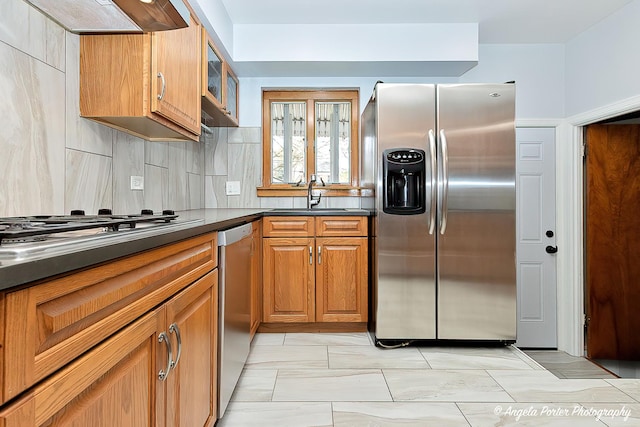 kitchen with dark countertops, a sink, brown cabinetry, stainless steel appliances, and tasteful backsplash