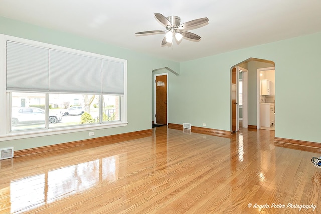 unfurnished living room with visible vents, wood finished floors, baseboards, ceiling fan, and arched walkways