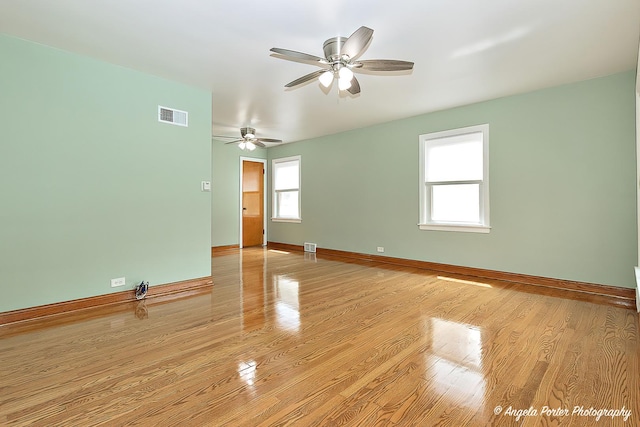 empty room featuring ceiling fan, visible vents, baseboards, and light wood finished floors