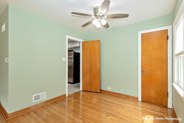 unfurnished bedroom featuring multiple windows, light wood finished floors, freestanding refrigerator, baseboards, and visible vents