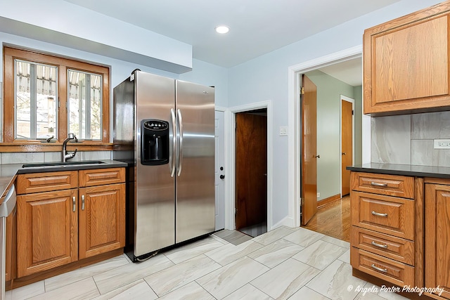 kitchen featuring brown cabinets, stainless steel refrigerator with ice dispenser, dark countertops, and a sink