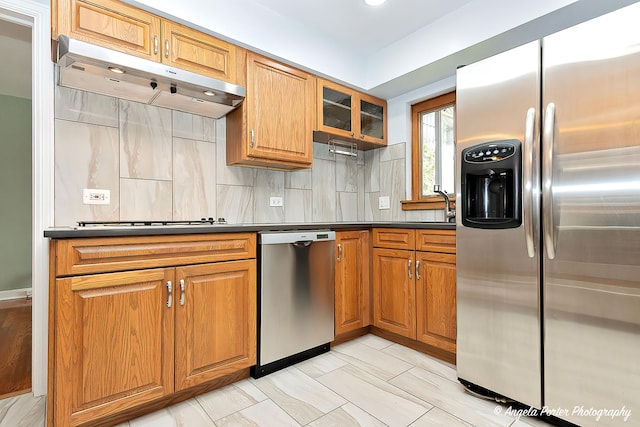 kitchen with decorative backsplash, under cabinet range hood, dark countertops, and stainless steel appliances