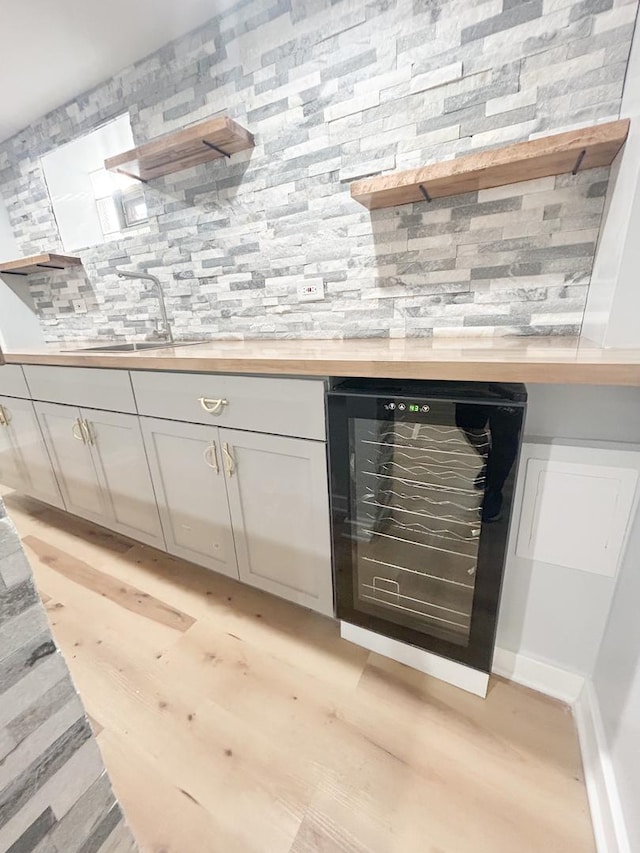 bar featuring tasteful backsplash, a sink, light wood-style floors, indoor wet bar, and wine cooler