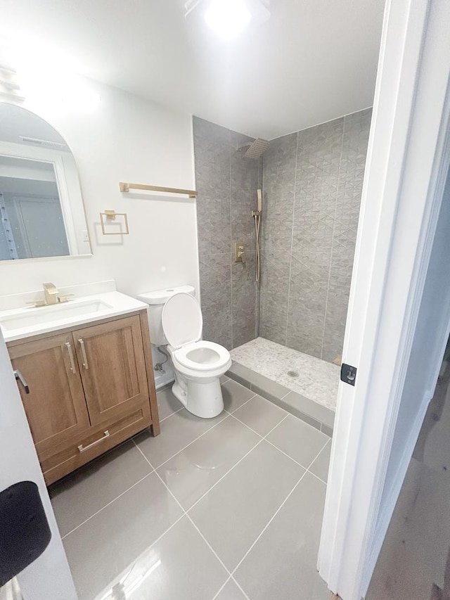 bathroom with toilet, a tile shower, tile patterned flooring, and vanity